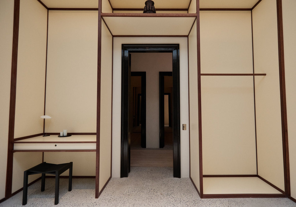 Minimalist interior with cream paneled walls and dark wood trim featuring a central doorway a built in desk and a black chair