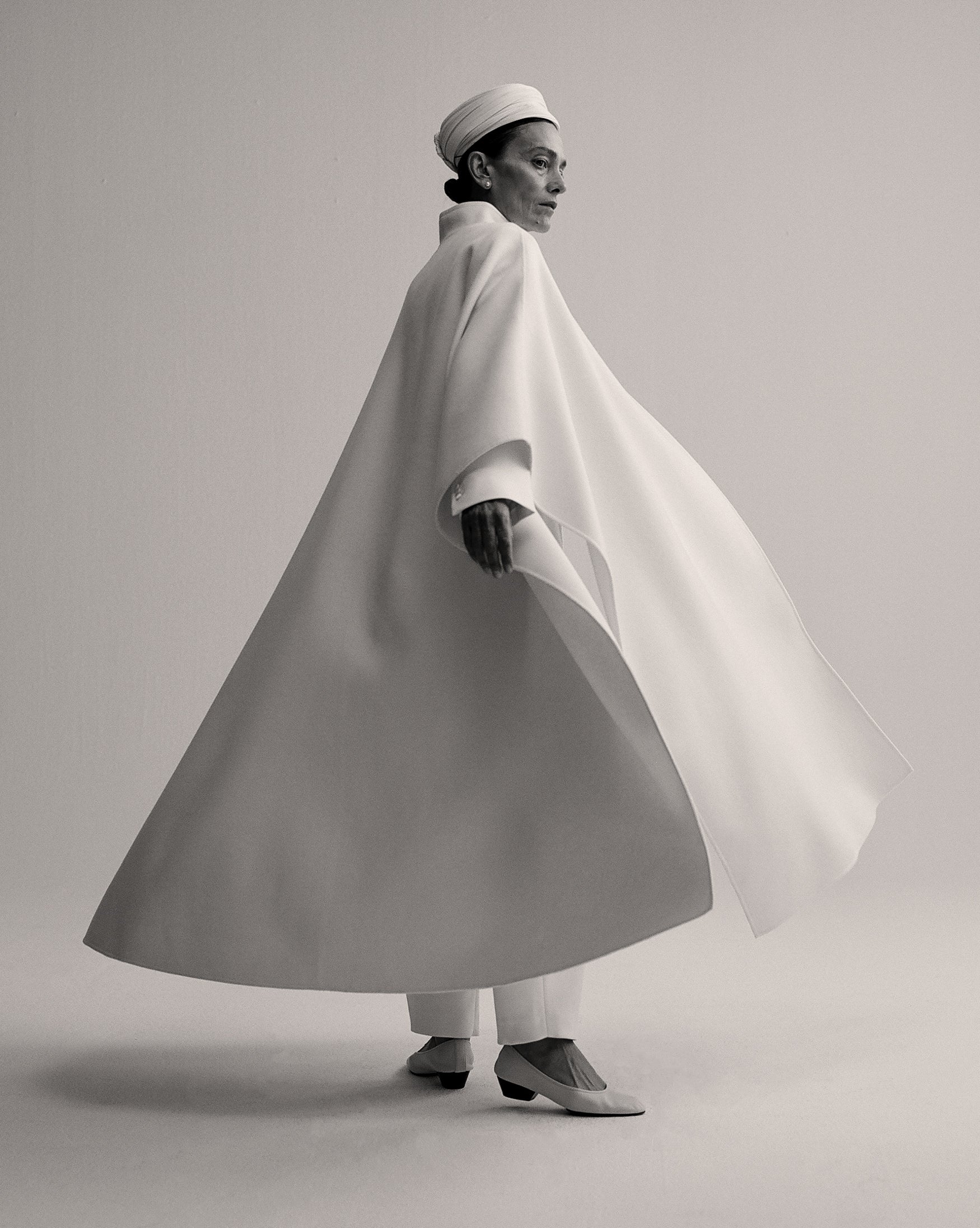 Woman wearing a white cape, turning around creating a wide shape. 