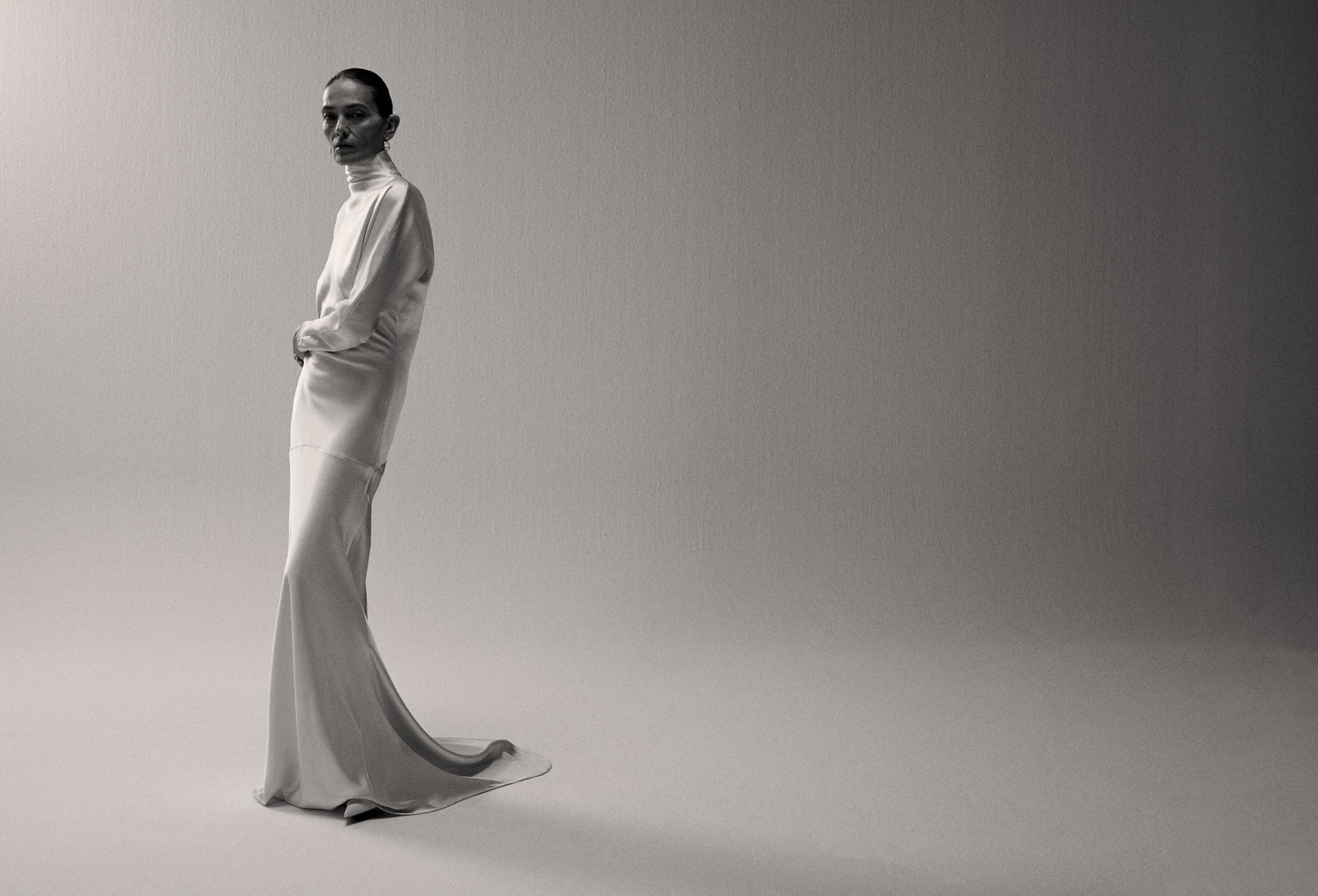 Woman in a satin long sleeve dress standing against a white backdrop.