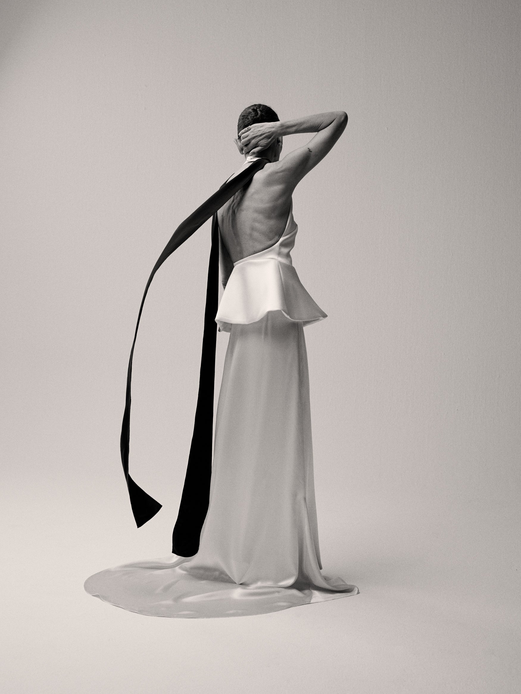 Woman in a satin long dress with a black scarf from the back against a white backdrop.