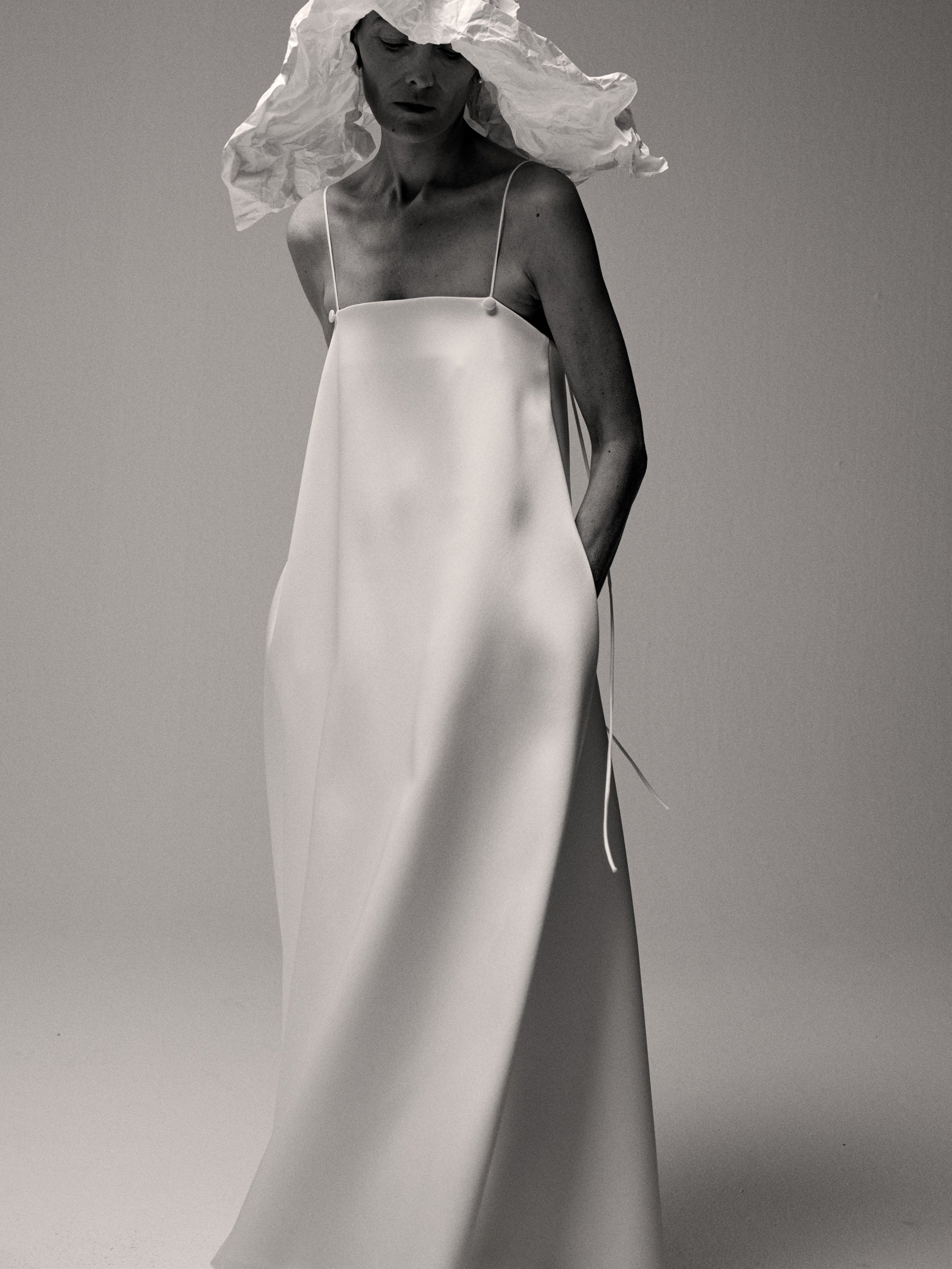 Woman a long white dress and crushed hat standing against a white backdrop.