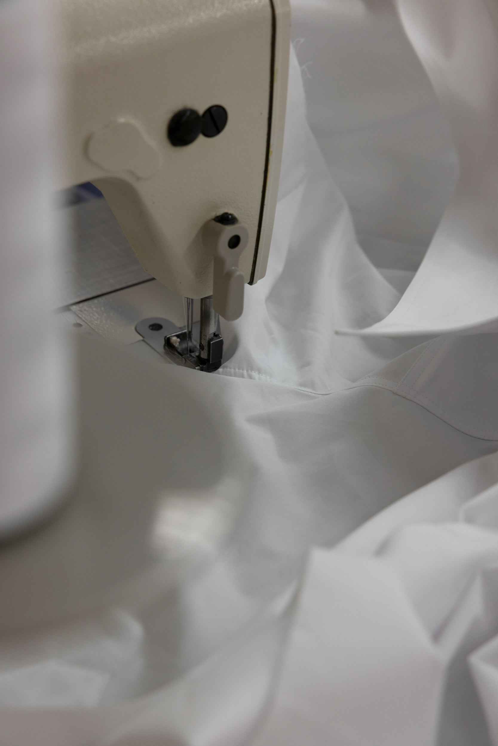 Close-up of a sewing machine needle on white cotton shirt fabric
