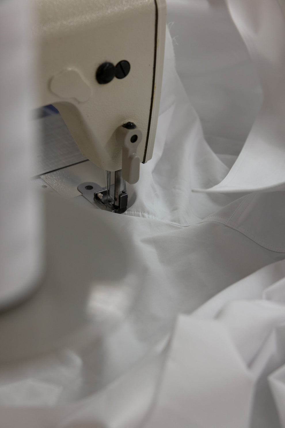 Close-up of a sewing machine needle on white cotton shirt fabric