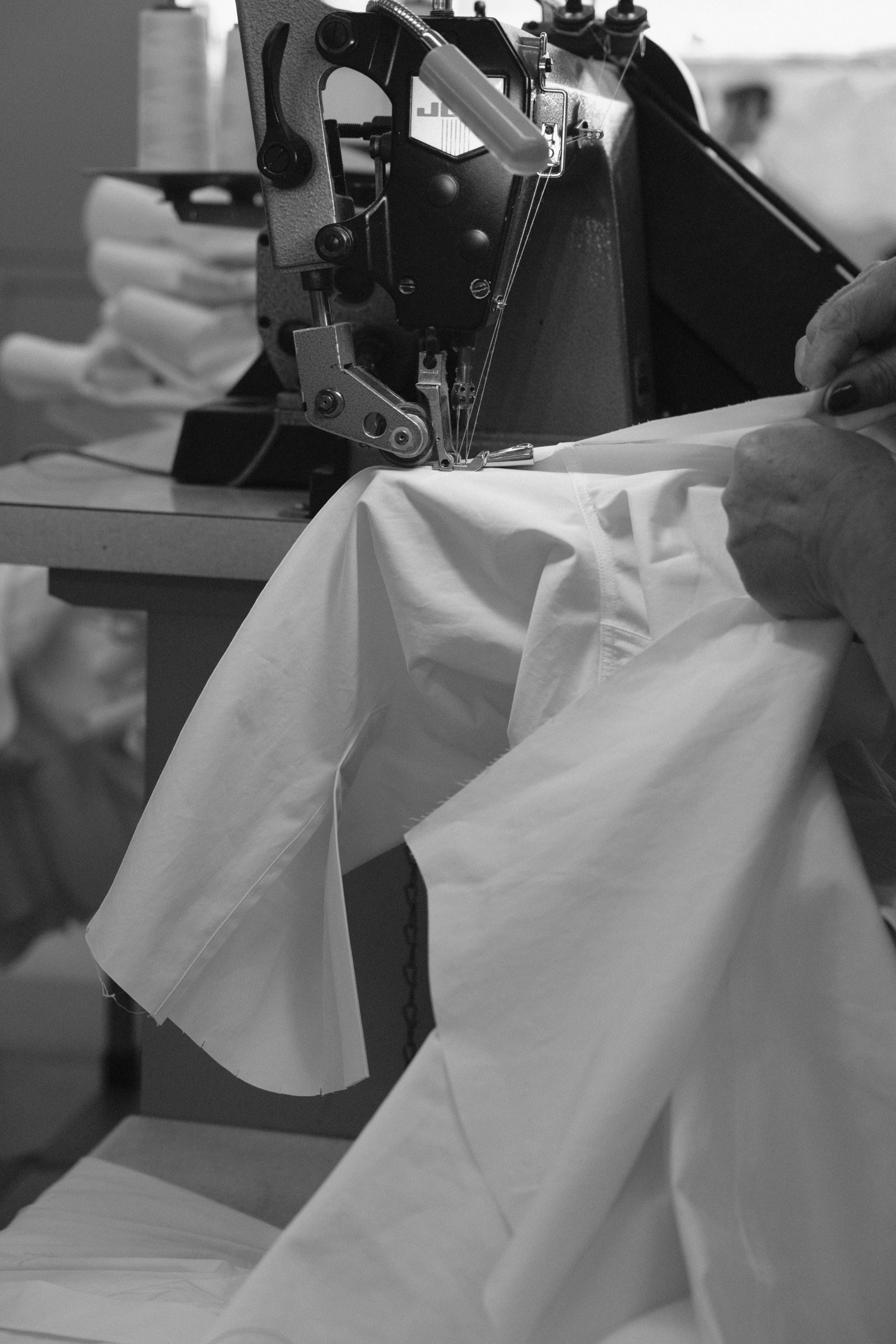 Person using a sewing machine to stitch the sleeves on a white shirt