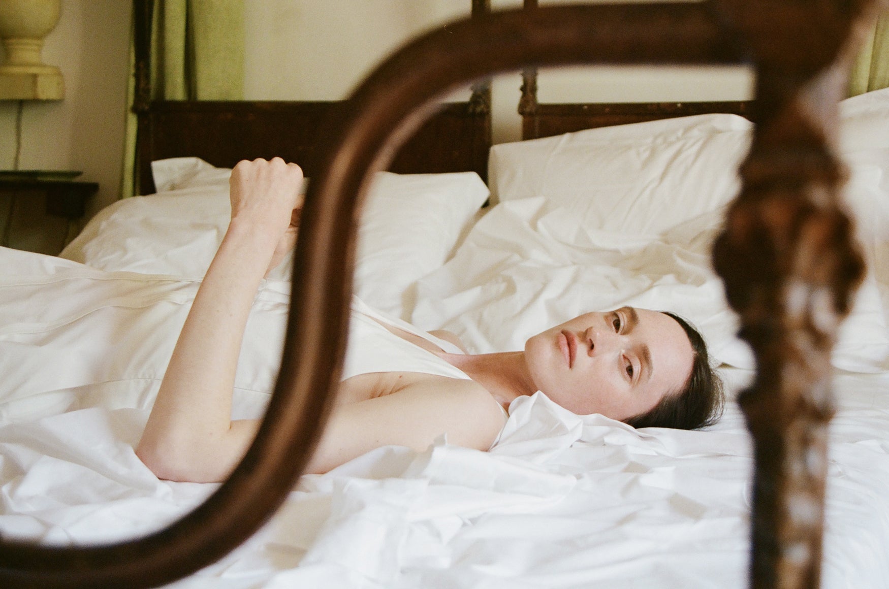 Woman in a white cotton poplin dress lying on a bed with white sheets