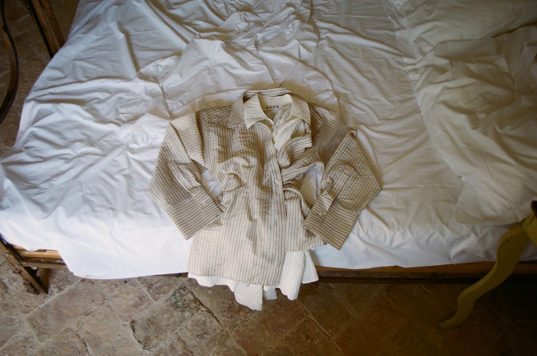 Beige and blue striped wrap shirt on a white bedspread with a stone floor in the background