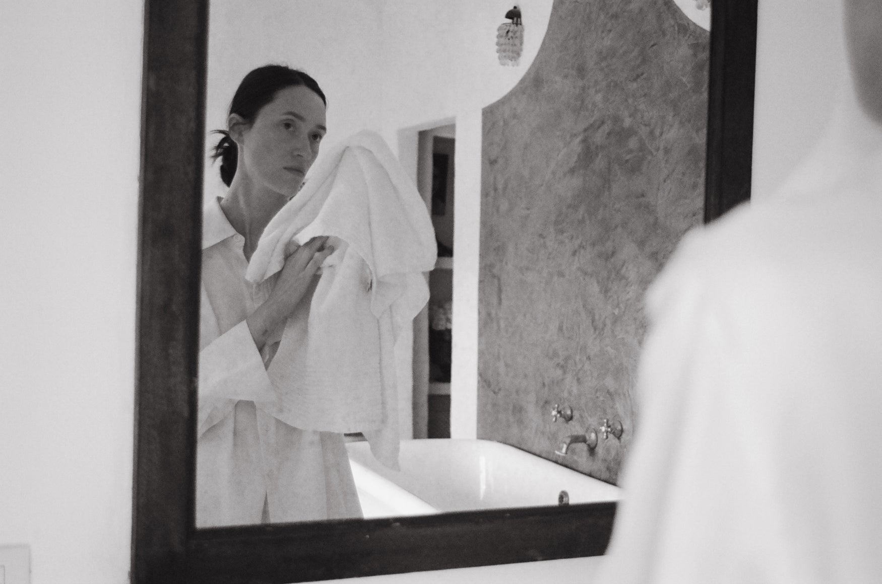 Woman drying her face holding a towel in front of a mirror in a bathroom.