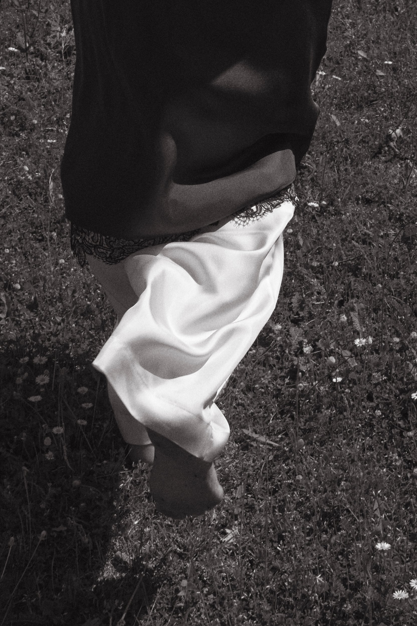 Woman running through a grass field wearing silk cream trousers with a silk skirt layered on top