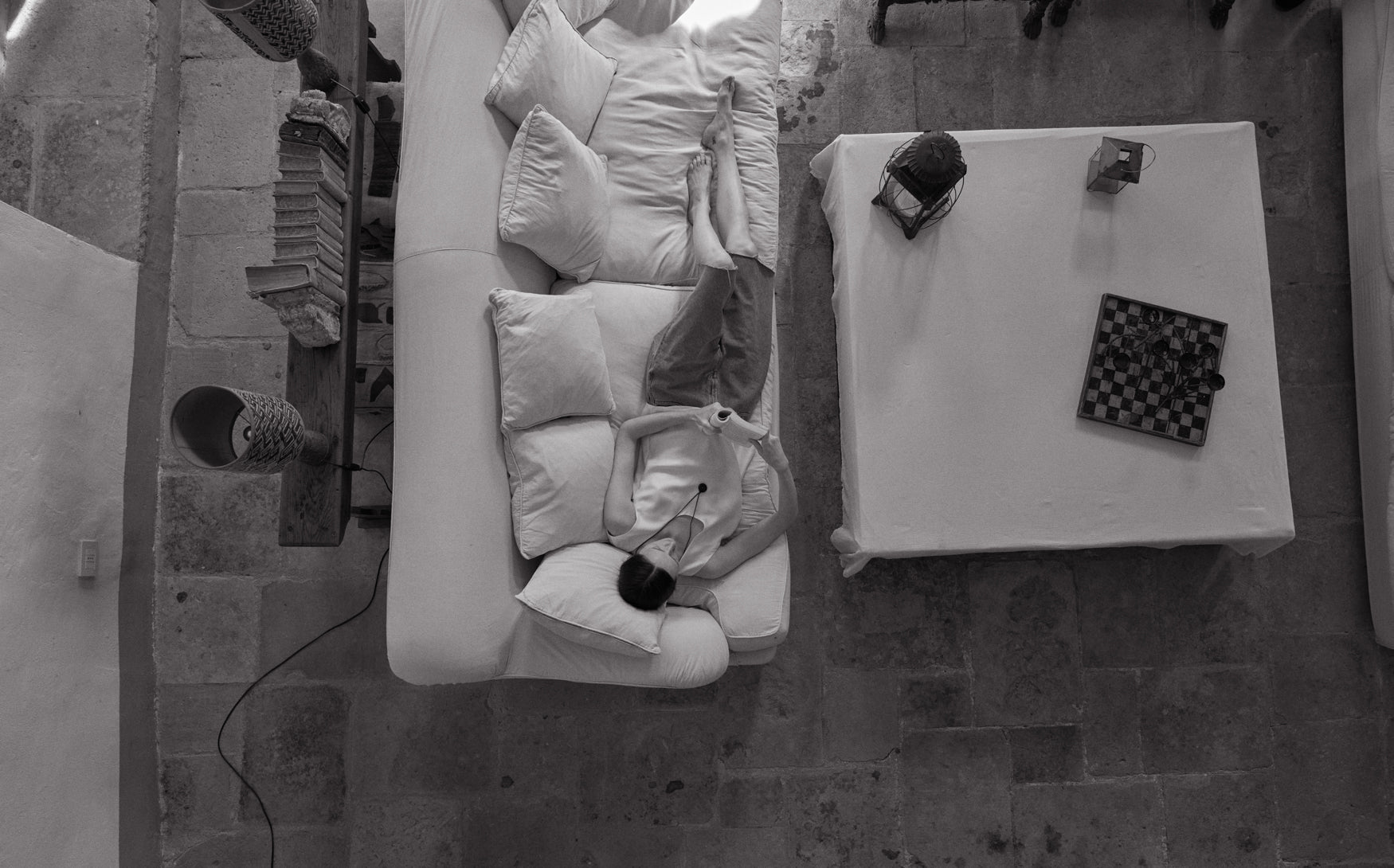 Black and white image of a room from above with a woman reading on a sofa, coffee table, and decorative items.