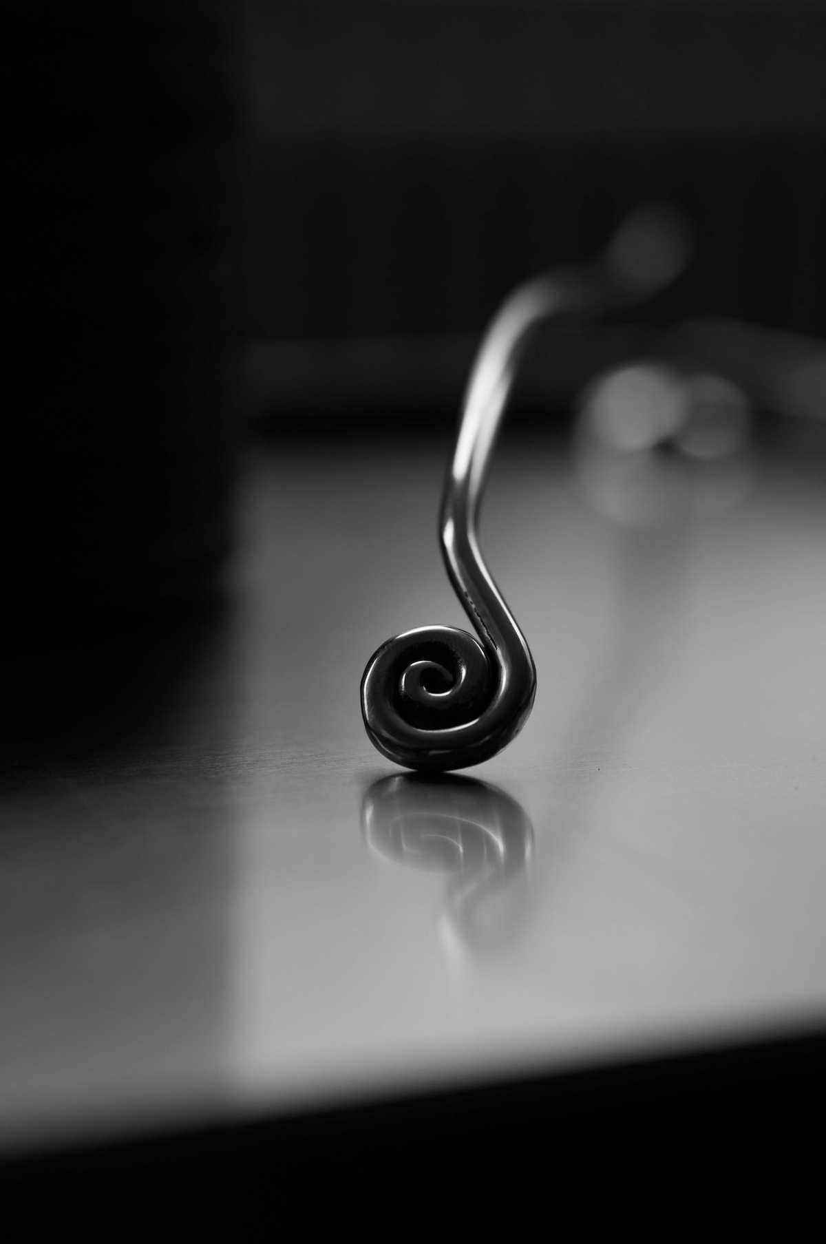 Close-up of Candle Stopper | silver, featuring a spiraled stainless steel handle resting on a reflective surface, highlighting its elegant, organic design for candle extinguishing.