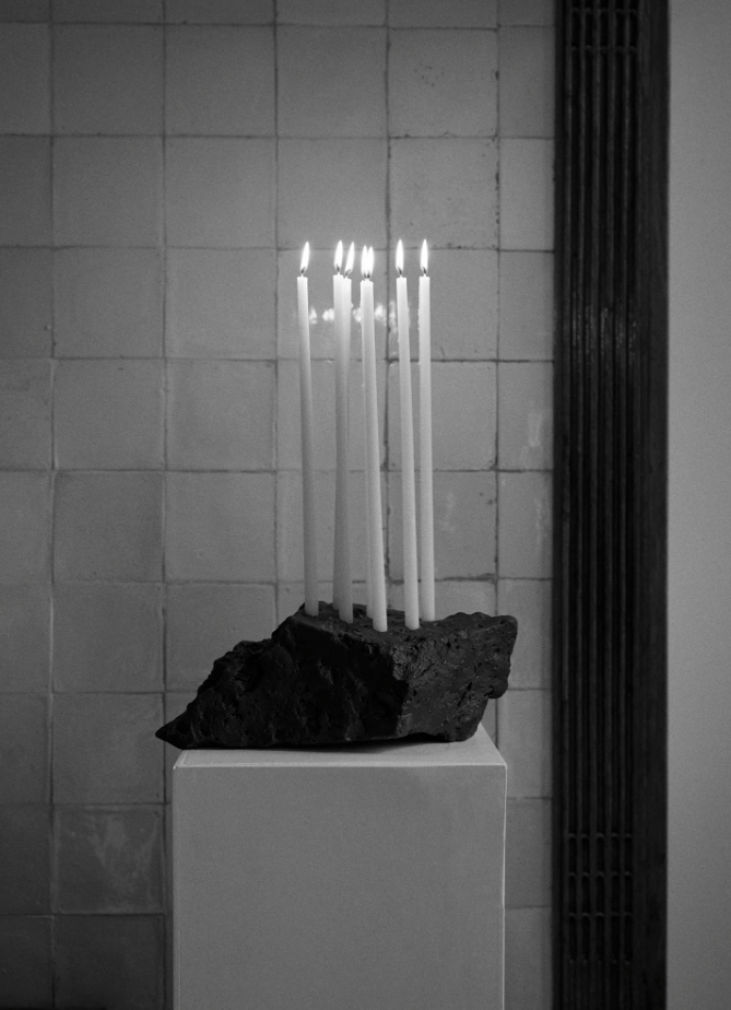 Black lava stone candleholder with 6 tall candles in it against a tiled backdrop