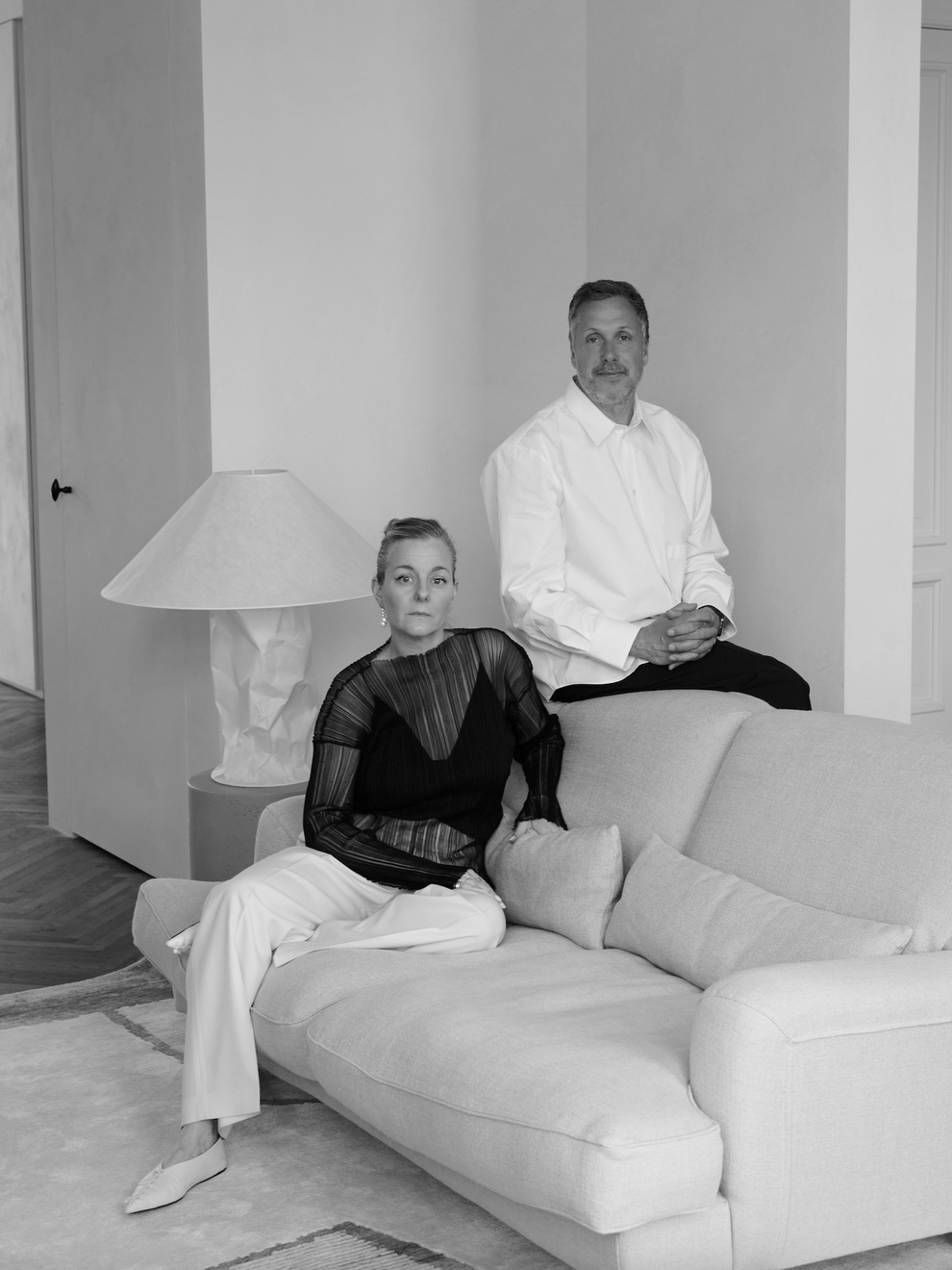 Black and white portrait of two people sitting on a couch in a modern living room.
