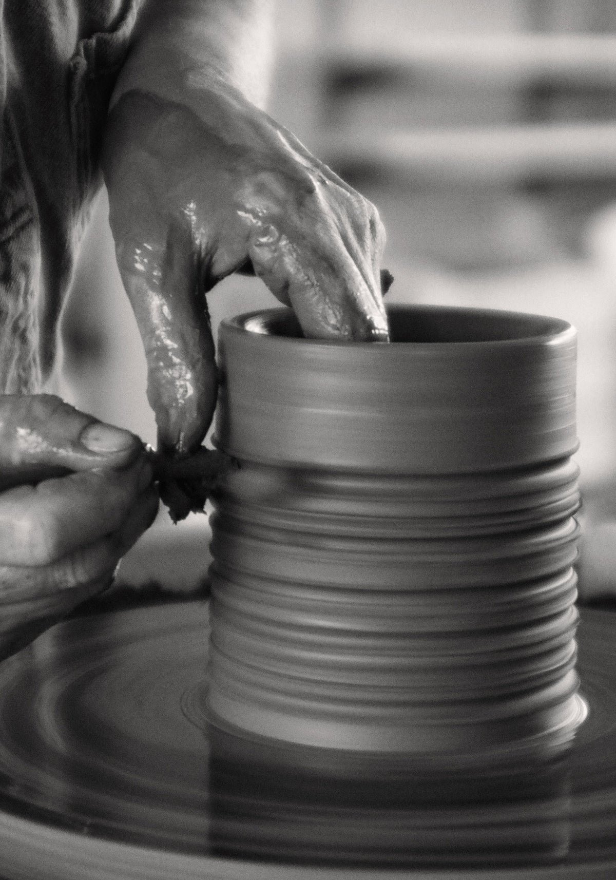 Close-up of hands shaping a textured clay vessel on a pottery wheel, illustrating the artisanal craftsmanship behind the Diplomatico Scented Candle | clay.