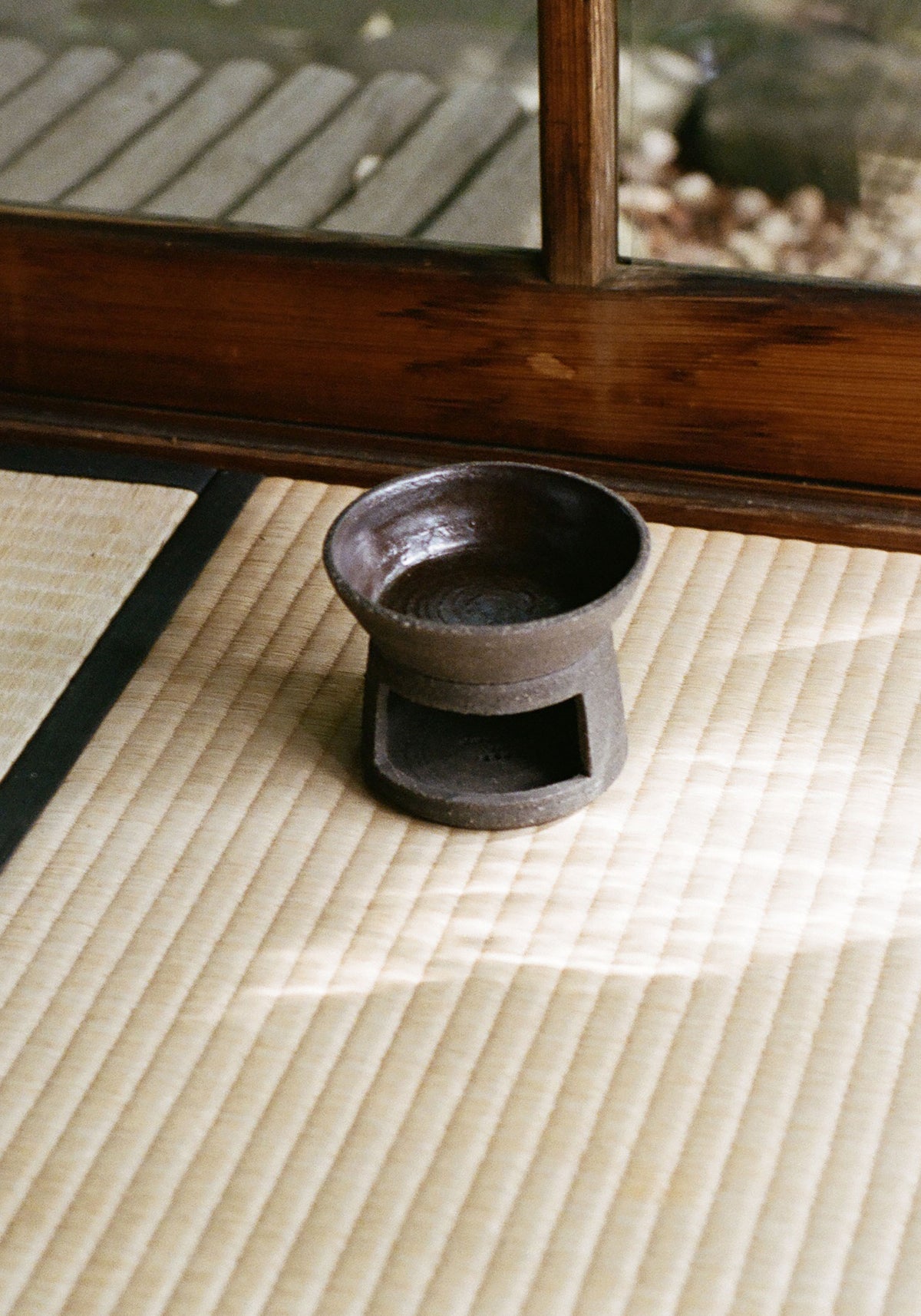 Ceramic Oil Burner | soil with a dark, rustic finish placed on a woven tatami mat next to a wooden framed glass door, showcasing a minimalist and natural aesthetic.
