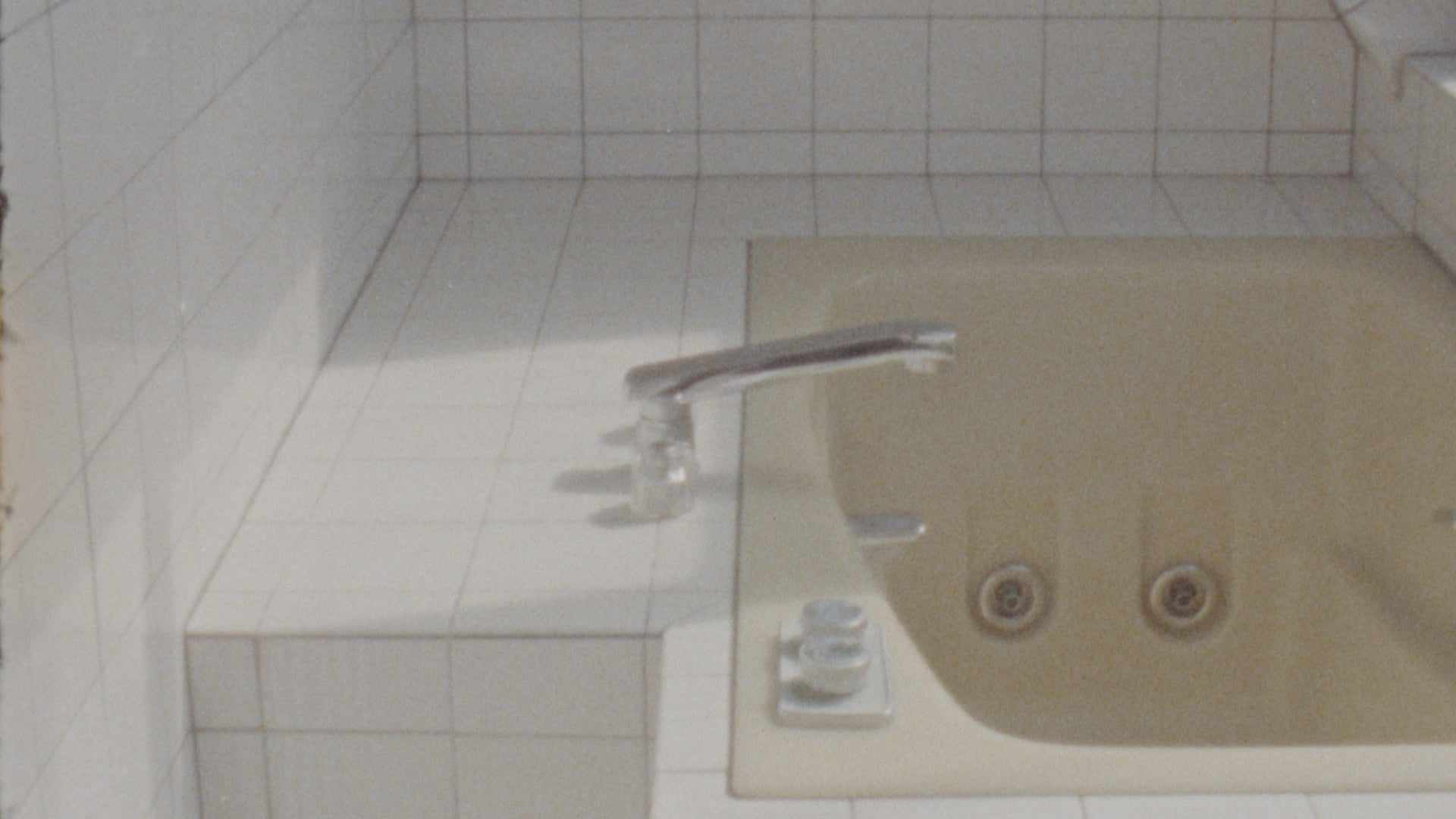 Image of a built-in yellow bath tub surrounded by white tiles 