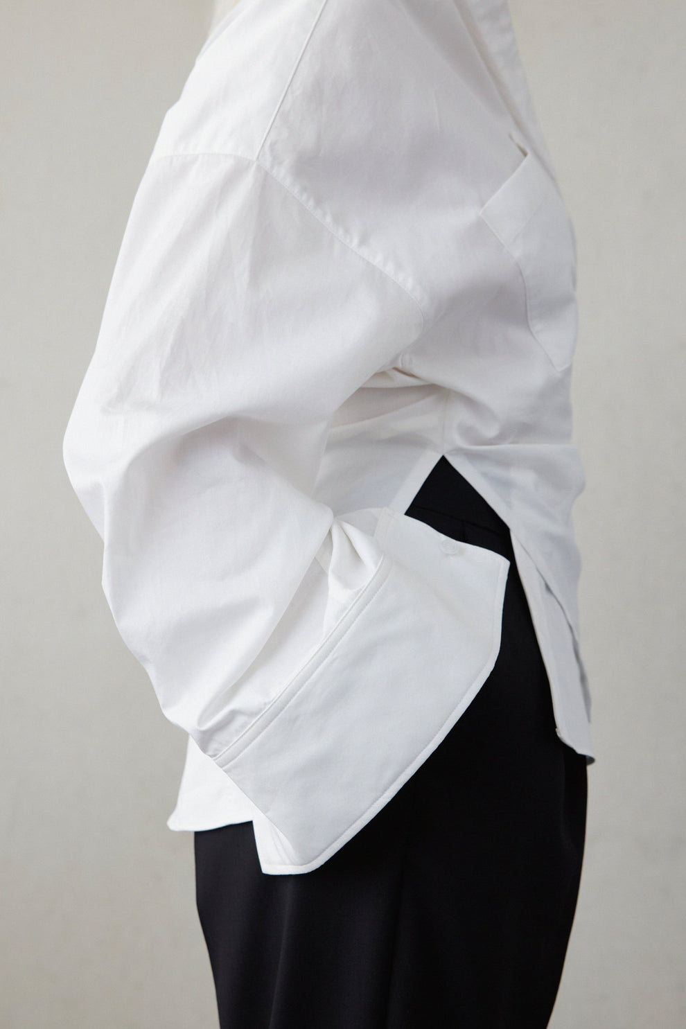 Woman wearing a white shirt with long wide sleeves and black pants on a plain background