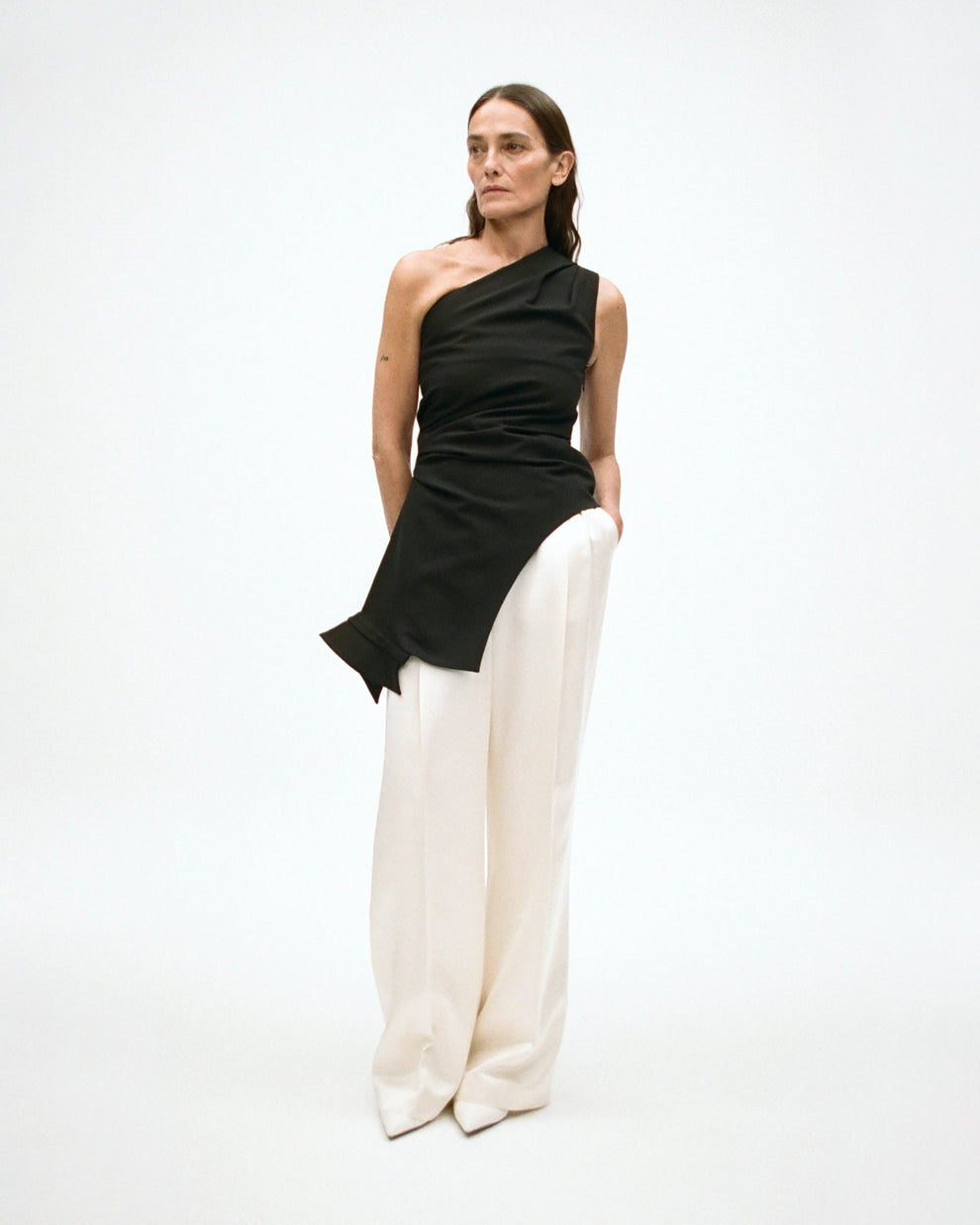 Woman wearing a black one-shoulder top with cream satin pants on a white background