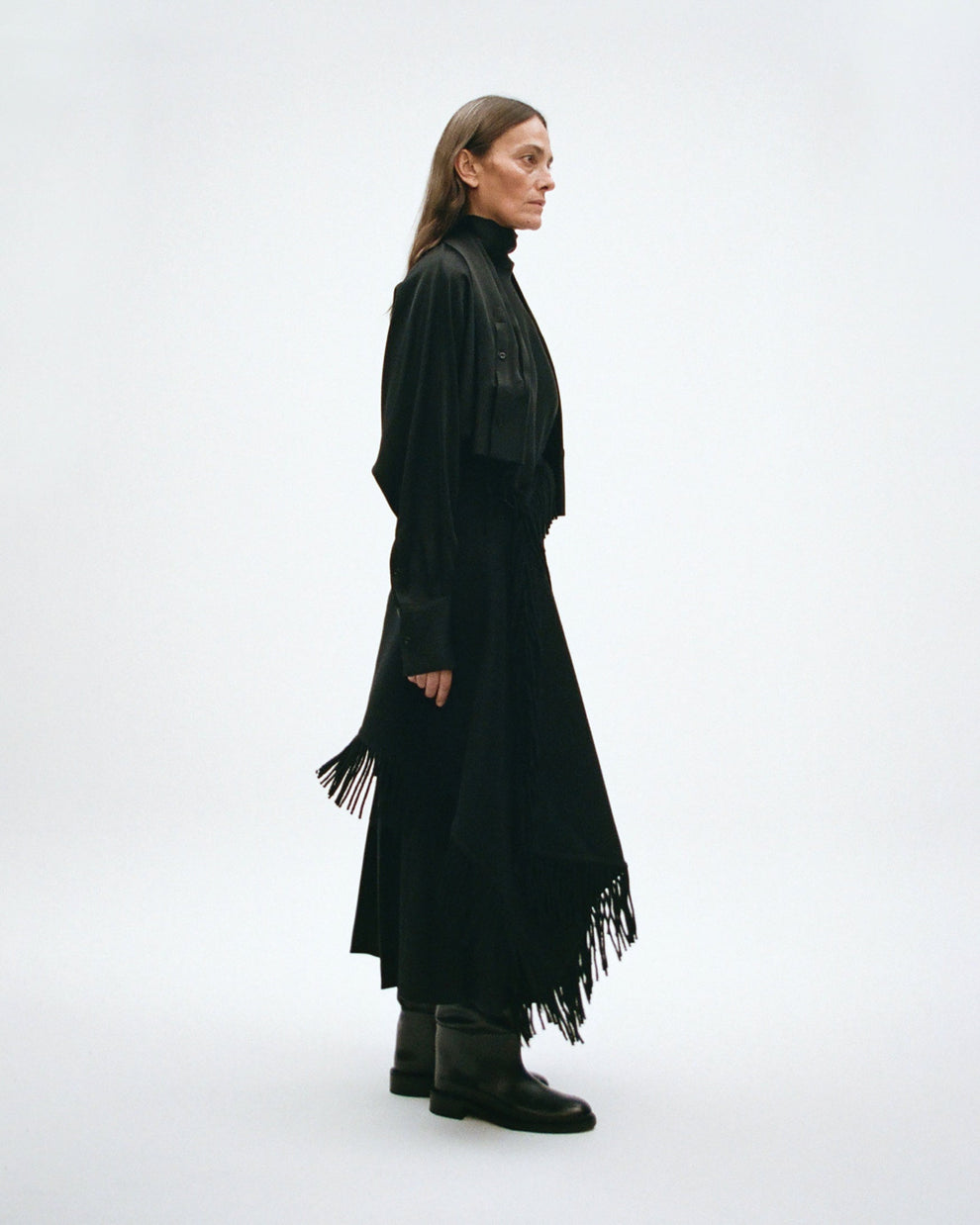 Woman wearing silk turtleneck top with a long black skirt with fringes on a white background
