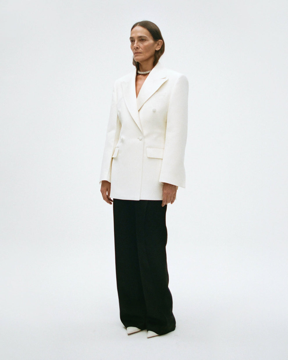Woman wearing an off-white blazer and black pants on a white background