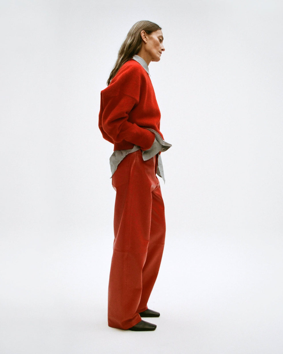 Woman wearing a red boiled wool pullover and red leather trousers with a white background