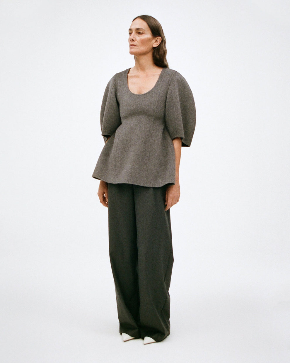 Woman wearing a gray double faced wool sculptural short sleeve top, and dark grey wide leg pants on a white background