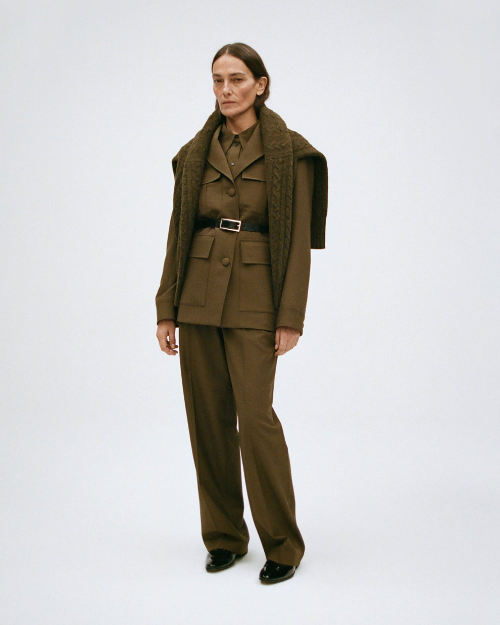 Woman wearing a forest green suit with a belt around the waist on a white background