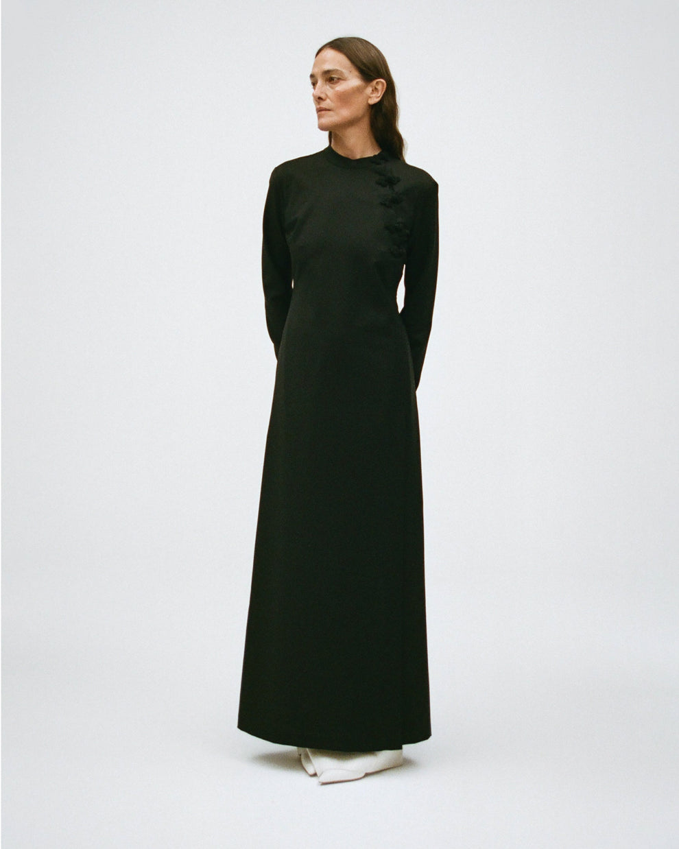 Woman wearing a long black dress with a high neckline and long sleeves on a white background